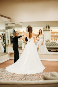 Aurora Bridal Boutique Stylist helping a bride with her dress try on.
