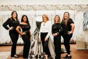 Aurora Bridal Boutique team posing in front of a gorgeous black and white bridal gown.
