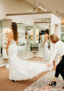 Aurora Bridal Boutique Bride trying on her wedding dress while owner, Cami Hester, spreads out her train behind her.