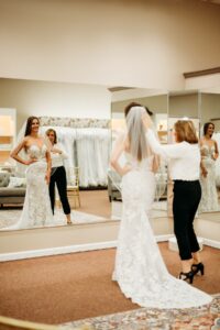 Aurora Bride to Be smiling at her reflection in the mirror at Aurora Bridal Boutique.