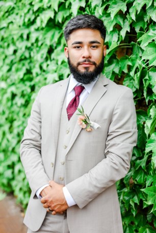 man posing in tuxedo in front of plant wall