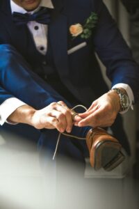 Aurora Bridal Boutique Groom wearing blue wedding suit and tying his shoes.