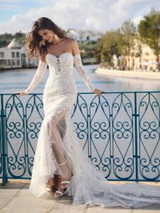 Lovely Aurora Bridal Bride wearing a lace dress and standing in front of a canal.