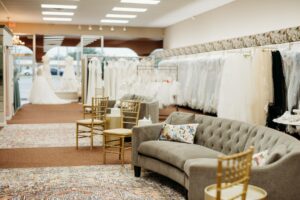 Inside seating area of Aurora Bridal Boutique. There are slightly curved grey couches with golden chairs seated on each end.