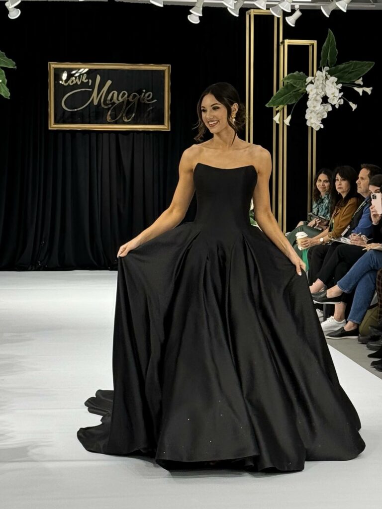 beautiful woman wearing a striking black dress for wedding, walking down a catwalk at Aurora Bridal