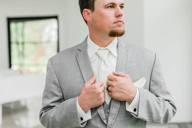 man holding his lapels as he wear a grey wedding suit at Aurora Bridal shop