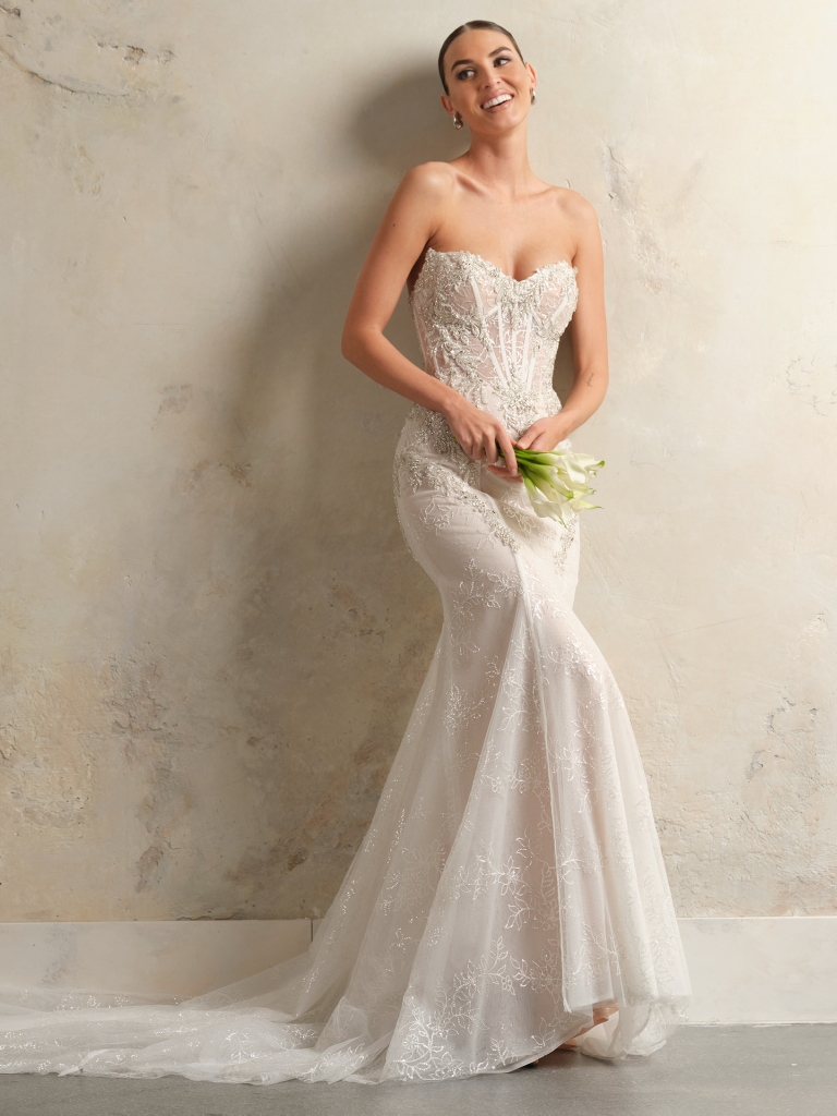 woman wearing a form-fitting, glamorous wedding dress and holding a small bouquet of green and white flowers