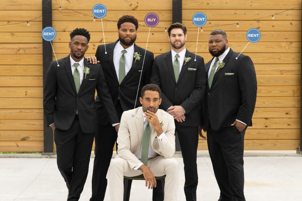 A group of men dressed in black tuxedos, posed around a groom dressed in a tan suit, all with green ties.