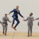 A group of four groomsmen posing around the groom who is jumping in a blue suit.