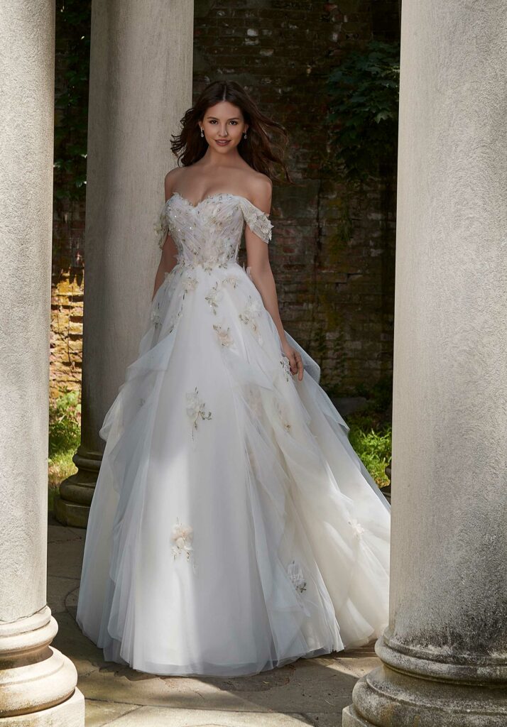 Bride wearing a floral-embroidered wedding gown, posing elegantly in front of white columns at a scenic outdoor venue.