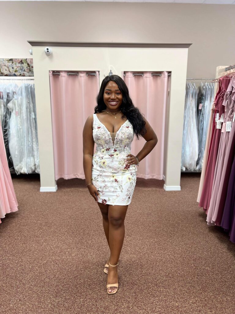 Bride smiling in a floral mini wedding dress, standing inside a beautifully lit bridal shop in Merritt Island.