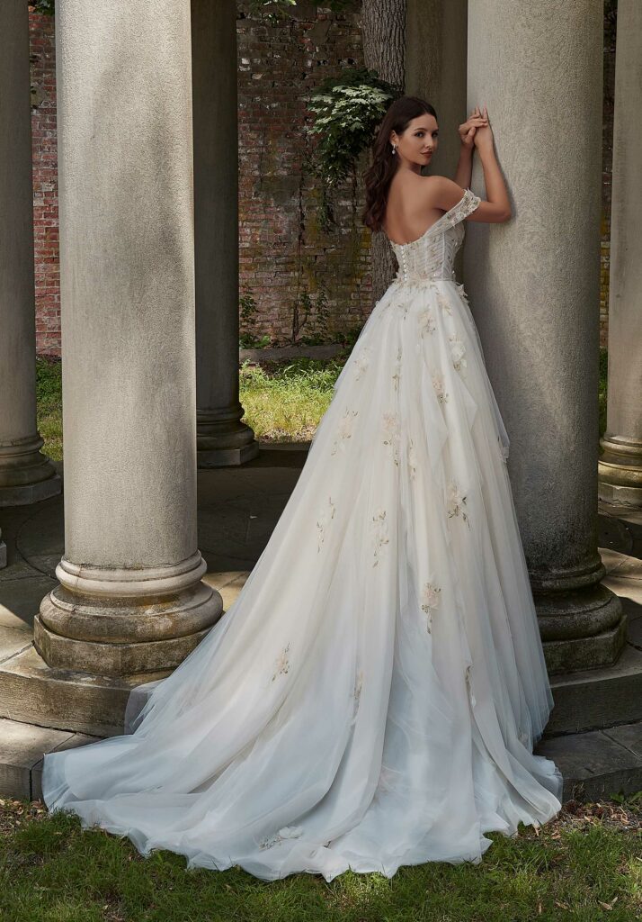 Bride in a flowing floral wedding gown posing by classical columns in a serene outdoor setting.