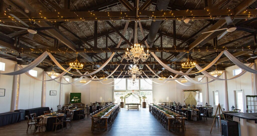 Grand barn interior with hanging lights, rustic chandeliers, and flowing drapery for a beautifully romantic reception.