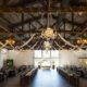 Grand barn interior with hanging lights, rustic chandeliers, and flowing drapery for a beautifully romantic reception.