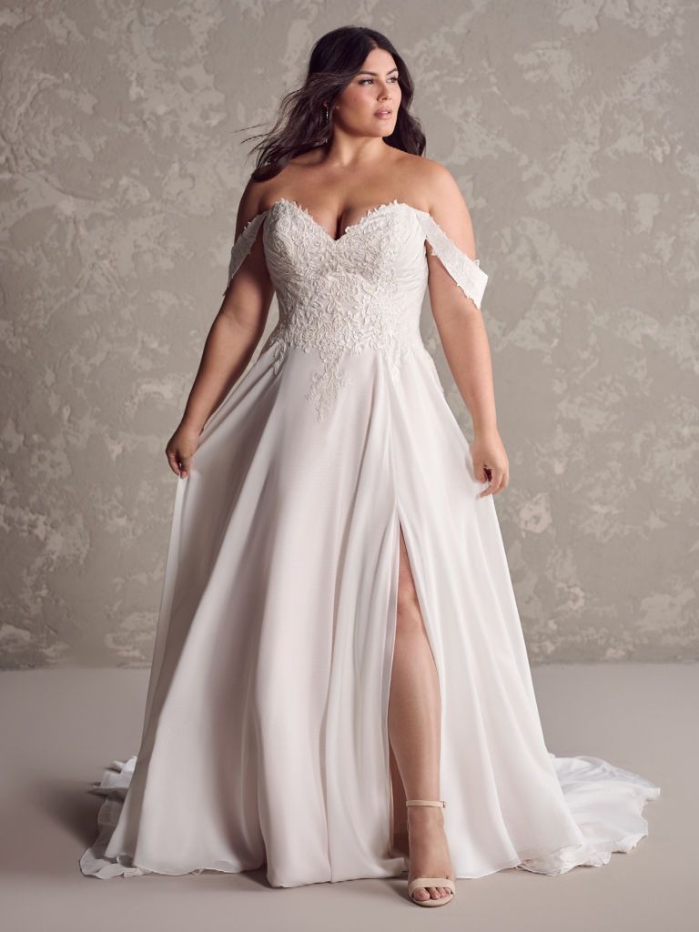 Bride wearing a romantic off-shoulder wedding gown with a flowy skirt, posed elegantly against a neutral studio background.