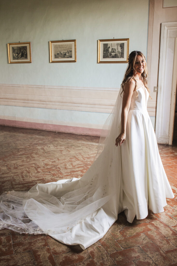 Bride standing in a vintage-inspired room with high ceilings and soft lighting, wearing a satin ballgown with button details.