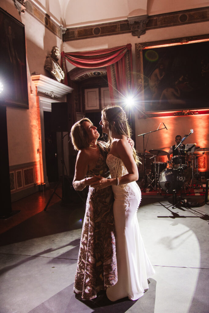 Bride dancing with her mother during the reception, both smiling in an elegant Italian wedding venue.