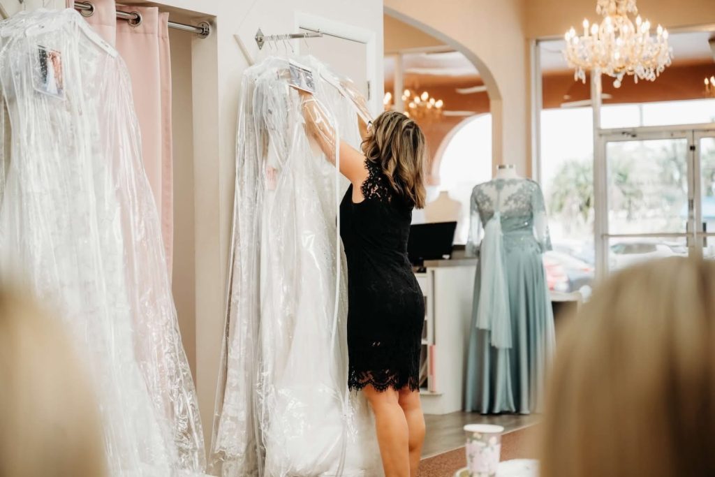 A bridal consultant at Aurora Bridal pulling a wedding dress from the rack while preparing for a bridal appointment in the showroom.