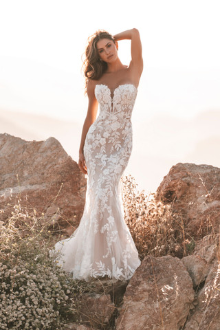 A bride poses confidently in a fitted strapless lace mermaid wedding dress, standing atop sunlit boulders with a breathtaking natural backdrop.