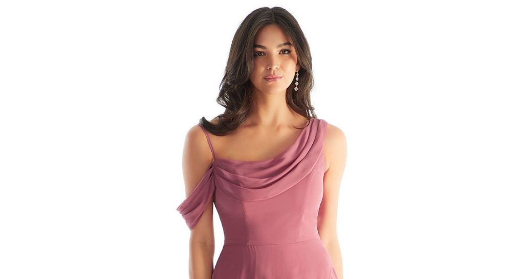A bridesmaid wears a flowing dusty rose gown with a draped cowl neckline and delicate off-the-shoulder sleeves, perfect for a spring wedding.