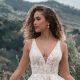 A bride poses in a romantic lace ballgown with a deep V-neck and delicate floral appliques, set against a stunning countryside landscape.