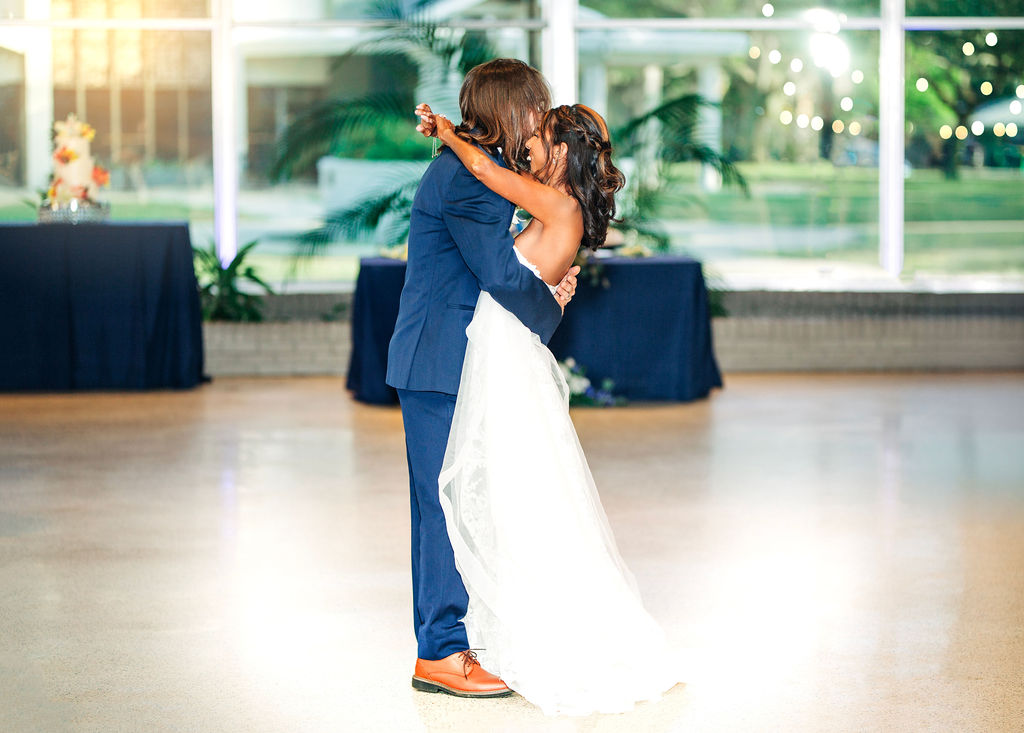 Bride and groom dance together in a bright reception hall, her veil flowing behind as they share a private moment.