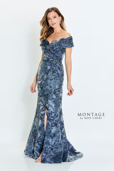 A woman in a slate blue floral lace gown with off-the-shoulder straps and a front slit, from the Montage by Mon Cheri collection.