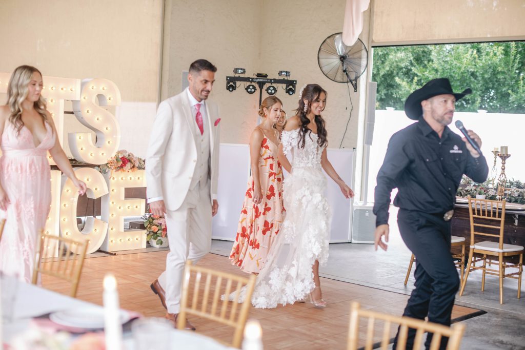 Wedding party learns a line dance led by an instructor in a cowboy hat at a reception.