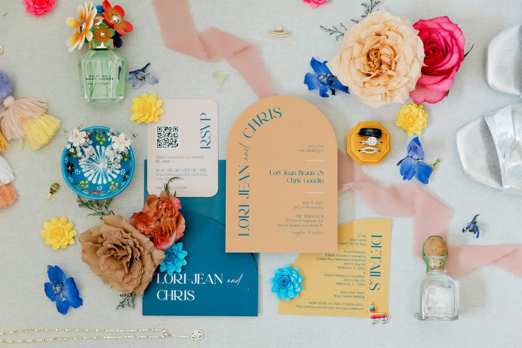 A flat lay of wedding invitations, flowers, jewelry, shoes, and small decorative items arranged on a light surface.