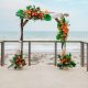 A closer view of a beachside wedding arch decorated with tropical flowers and greenery, flanked by metal cactus sculptures.