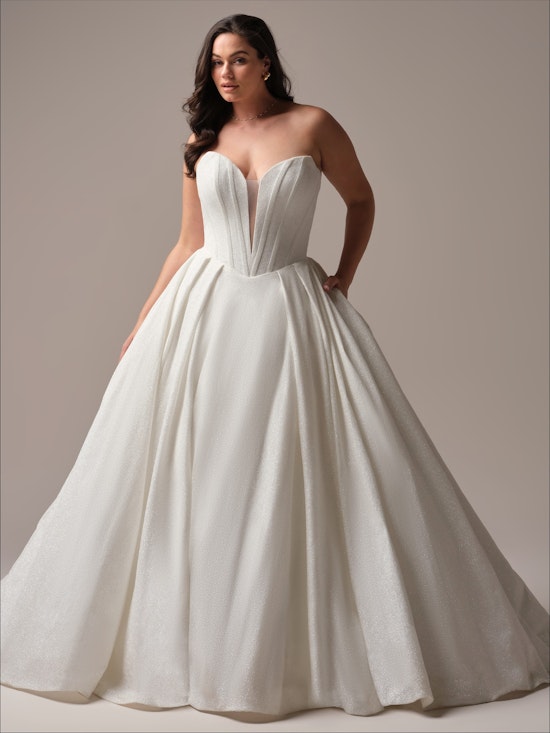 A bride poses in a strapless ballgown with a plunging neckline and full skirt, standing in a neutral studio space.