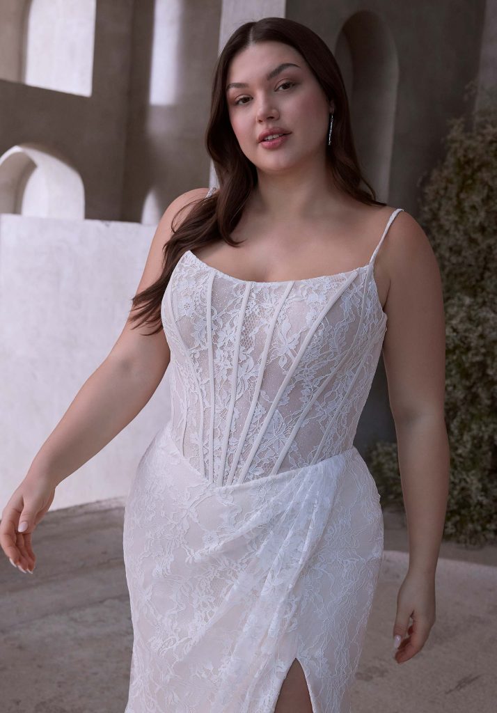 Close-up of a bride in a spaghetti strap lace wedding gown with boning details and a slit in the skirt.
