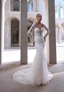 Bride in a fitted lace gown with long sleeves and a chapel-length train, posing among stone arches.