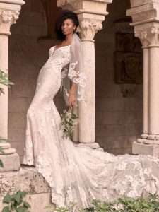 Bride in a lace mermaid wedding dress posing outdoors beside stone columns.