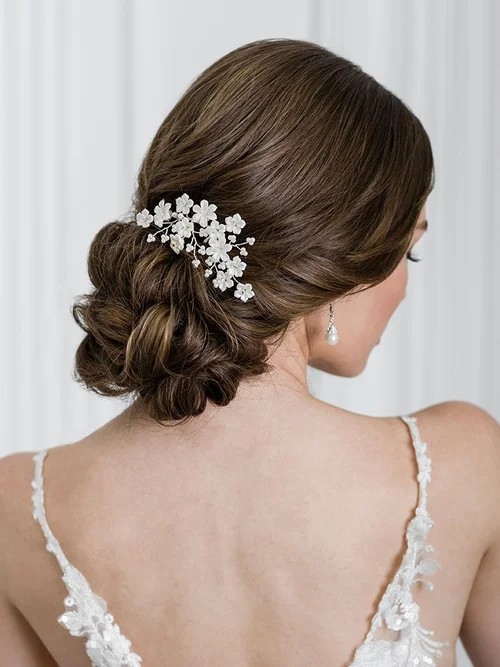 A bride’s hair is styled in a low, textured bun adorned with delicate white floral hairpins, shown from the back.
