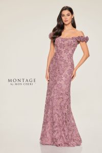 A woman in an off-the-shoulder mauve lace gown poses against a plain background, her long dark hair styled in soft waves.