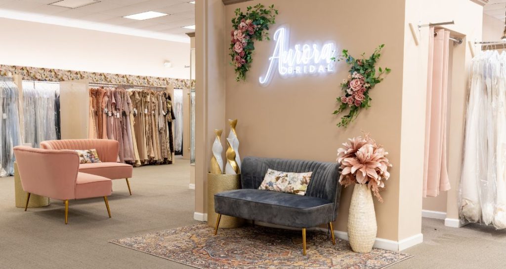 A cozy seating area inside a bridal shop featuring sofas, decorative pillows, and a glowing wall sign.