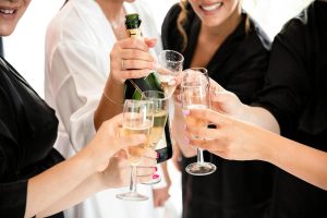 A group of women in robes raise champagne flutes together while smiling during a wedding celebration moment.