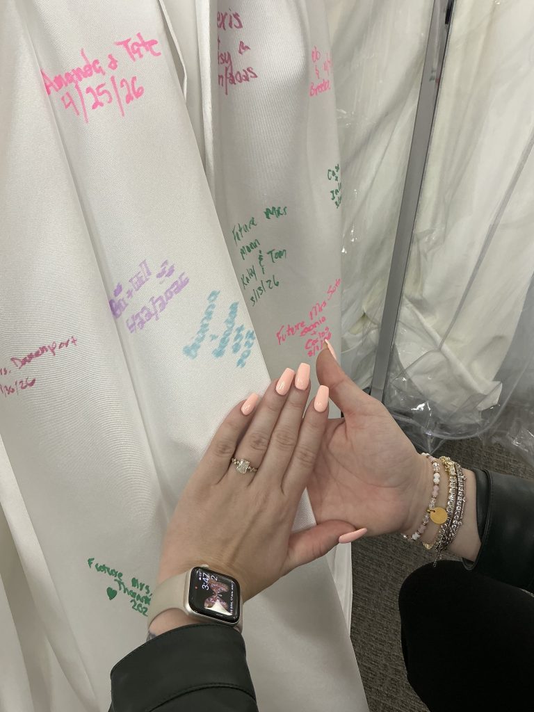 A close-up of hands with an engagement ring held up in front of a signed wedding dress.