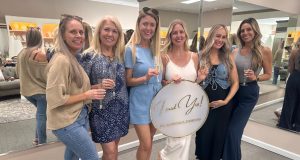 A group of women pose together indoors holding an “I said yes” sign and champagne glasses.