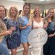 A group of women pose together indoors holding an “I said yes” sign and champagne glasses.