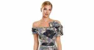 Woman wearing a gray off-the-shoulder floral evening gown photographed from the waist up against a plain background.