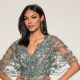 A woman wears a sage green embroidered gown with sheer flutter sleeves and beaded detailing against a neutral background.