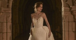 Bride in a strapless lace wedding gown with a sweetheart neckline and detachable overskirt, posing beneath a stone arch.