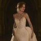 Bride in a strapless lace wedding gown with a sweetheart neckline and detachable overskirt, posing beneath a stone arch.