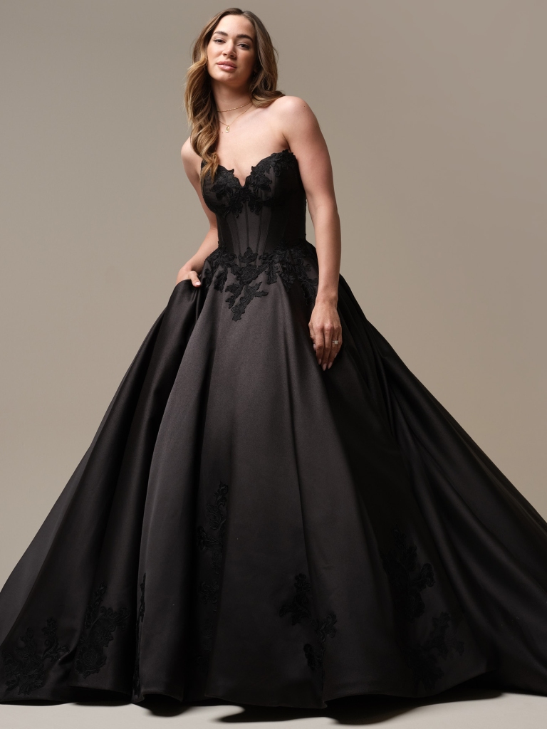 Bride wearing a strapless black ball gown with a fitted bodice and floral appliqué, posing in a studio with a full skirt.