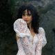 Woman with curly dark hair posing in a fitted lace wedding dress with puff sleeves in front of rocky ruins.