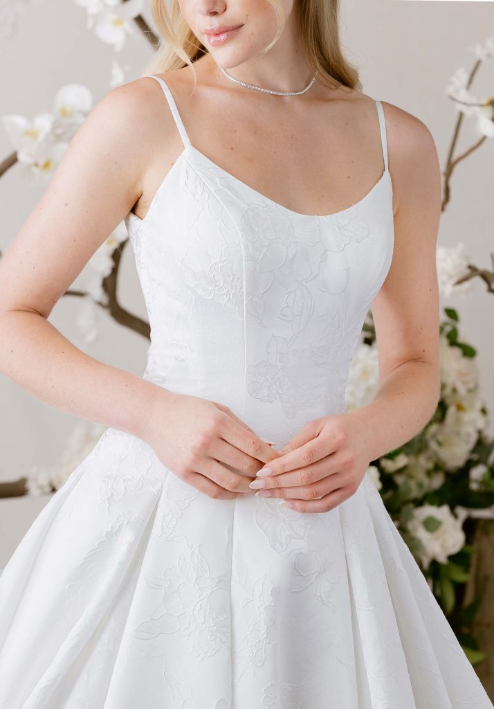 Close-up of a bride wearing a white floral jacquard wedding dress with thin straps and a delicate necklace.
