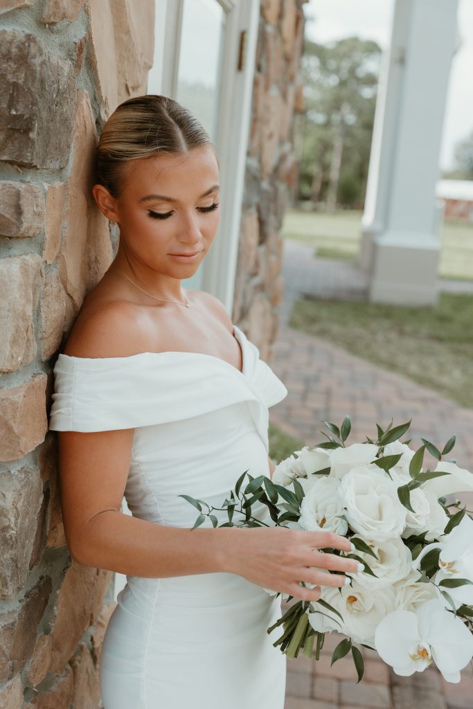 Bride in an off-the-shoulder wedding dress holding a bouquet of white roses and orchids.