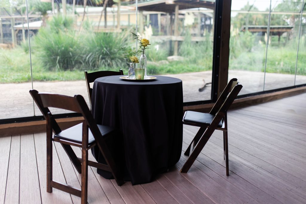 An indoor event area features black-covered cocktail tables next to an animal viewing area.